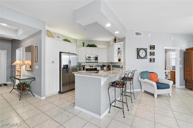 kitchen featuring a kitchen bar, kitchen peninsula, backsplash, stainless steel appliances, and white cabinetry