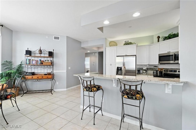 kitchen featuring stainless steel appliances, light stone counters, kitchen peninsula, a kitchen bar, and white cabinets