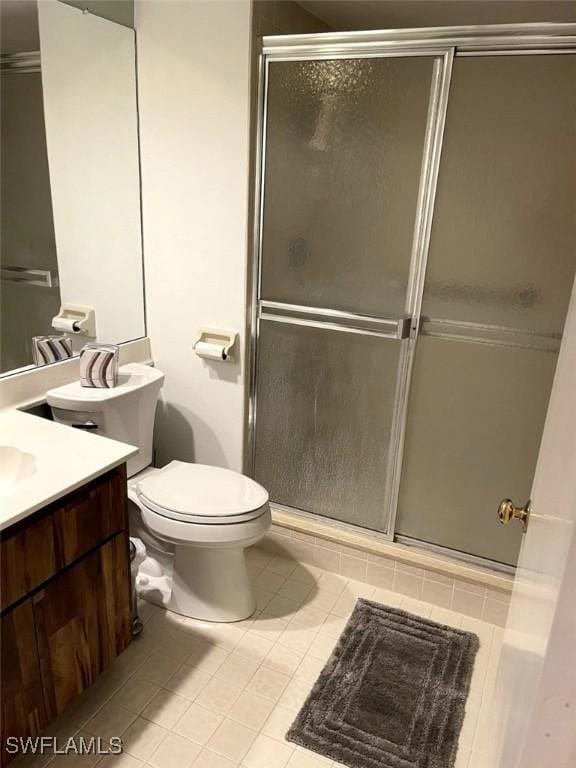 bathroom featuring tile patterned flooring, vanity, toilet, and a shower with door