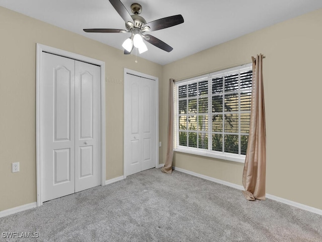 unfurnished bedroom with ceiling fan, light colored carpet, and two closets