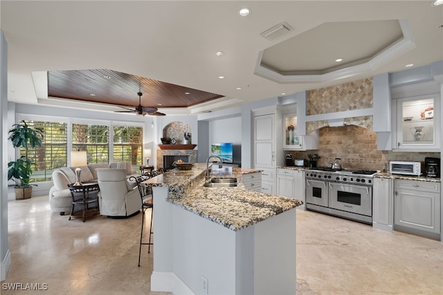 kitchen featuring white cabinets, range with two ovens, sink, a tray ceiling, and tasteful backsplash