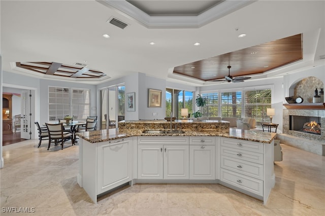 kitchen with stone counters, ceiling fan, a tray ceiling, a kitchen island with sink, and white cabinets