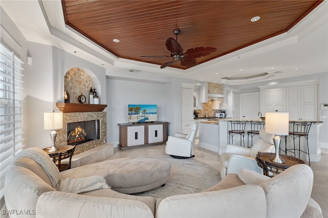 living room featuring ceiling fan, wood ceiling, a high end fireplace, and a tray ceiling