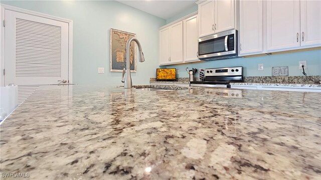 kitchen featuring stainless steel appliances, light stone counters, white cabinetry, and sink