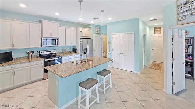 kitchen with a center island with sink, pendant lighting, light stone counters, and stainless steel appliances