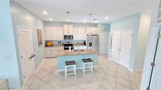 kitchen featuring a center island with sink, white cabinets, light stone countertops, and stainless steel appliances