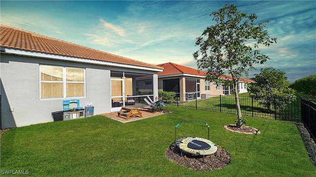 rear view of house featuring a sunroom, a yard, and an outdoor fire pit