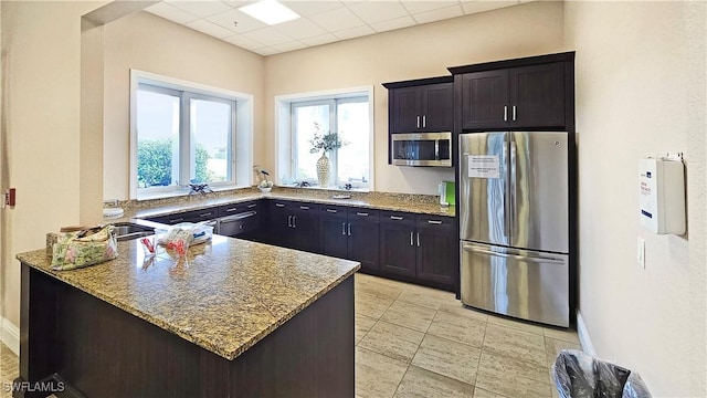 kitchen with dark brown cabinets, light stone counters, kitchen peninsula, and stainless steel appliances