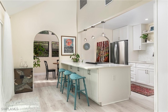 kitchen featuring white cabinetry, tasteful backsplash, light hardwood / wood-style flooring, stainless steel fridge, and a breakfast bar