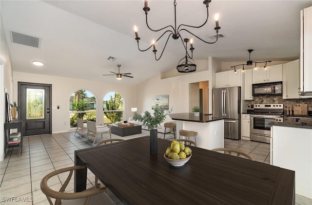 tiled dining room with a healthy amount of sunlight, ceiling fan with notable chandelier, and lofted ceiling