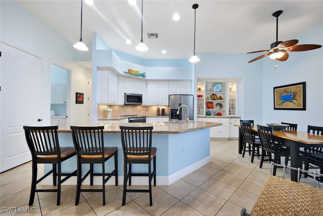 kitchen featuring a large island with sink, white cabinets, decorative backsplash, light stone counters, and stainless steel appliances