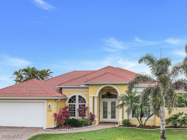 mediterranean / spanish-style home with a tile roof, stucco siding, french doors, decorative driveway, and a garage