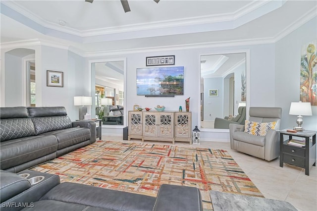 living room with light tile patterned floors, a tray ceiling, ceiling fan, and ornamental molding