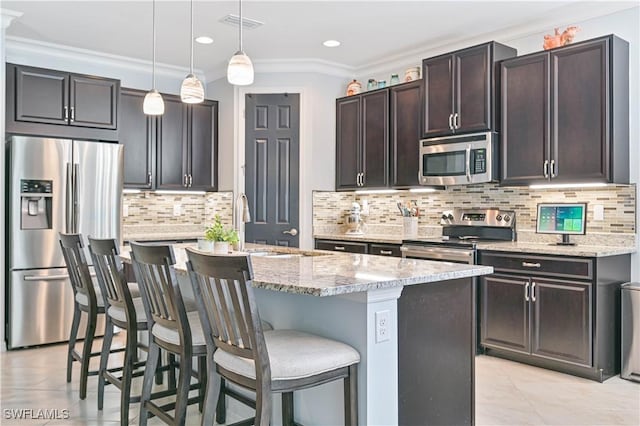 kitchen with ornamental molding, a kitchen island with sink, appliances with stainless steel finishes, and a breakfast bar area