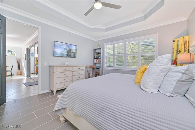 tiled bedroom with a tray ceiling, multiple windows, ceiling fan, and ornamental molding