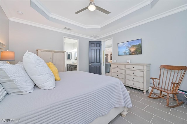 bedroom with ceiling fan, ornamental molding, connected bathroom, and a tray ceiling