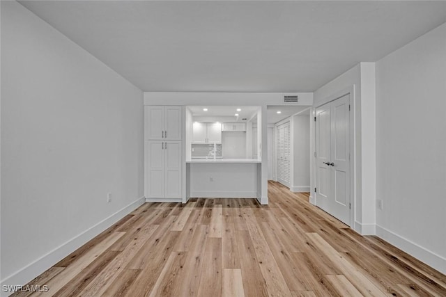 unfurnished living room with light wood-type flooring, visible vents, and baseboards