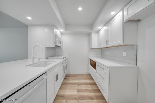 kitchen featuring light countertops, light wood-style flooring, white cabinets, a sink, and white appliances