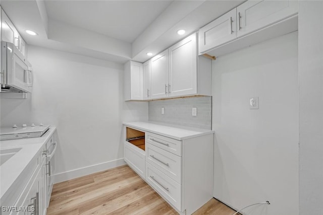 kitchen featuring backsplash, white microwave, white cabinetry, light wood-type flooring, and baseboards