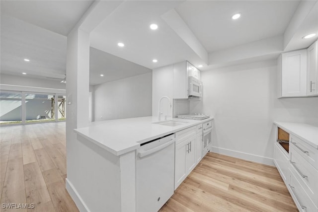 kitchen with a peninsula, white appliances, ceiling fan, and light wood finished floors