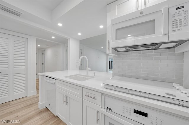 kitchen with visible vents, light wood-style flooring, white cabinets, a sink, and white appliances