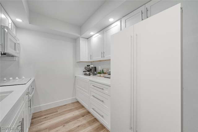 kitchen featuring white appliances, light wood finished floors, baseboards, light countertops, and white cabinetry