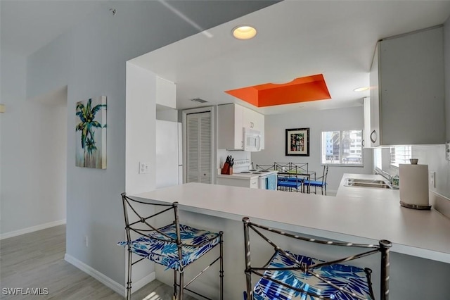 kitchen with kitchen peninsula, white appliances, white cabinetry, and sink