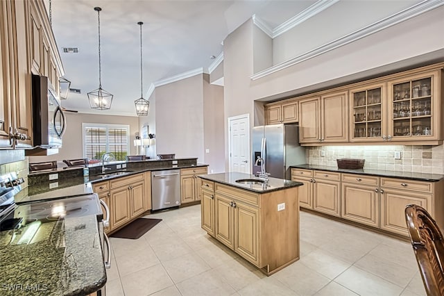 kitchen with backsplash, dark stone counters, stainless steel appliances, decorative light fixtures, and a center island with sink