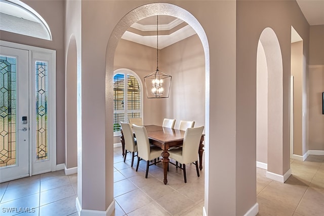 dining space with light tile patterned flooring, a raised ceiling, ornamental molding, and an inviting chandelier