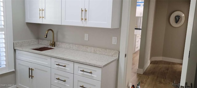 bar with wood-type flooring, light stone countertops, white cabinetry, and sink