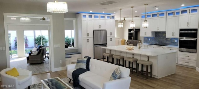 kitchen with white cabinetry, a kitchen breakfast bar, decorative light fixtures, a kitchen island with sink, and appliances with stainless steel finishes