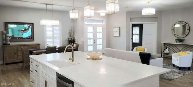 kitchen featuring a kitchen island with sink, sink, white cabinets, and hanging light fixtures