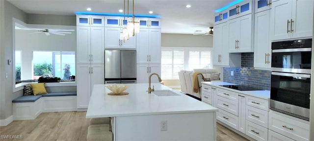 kitchen featuring pendant lighting, a kitchen island with sink, sink, appliances with stainless steel finishes, and tasteful backsplash