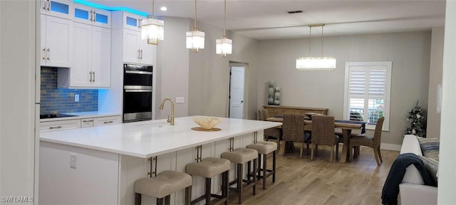 kitchen featuring white cabinetry, sink, hanging light fixtures, double oven, and decorative backsplash