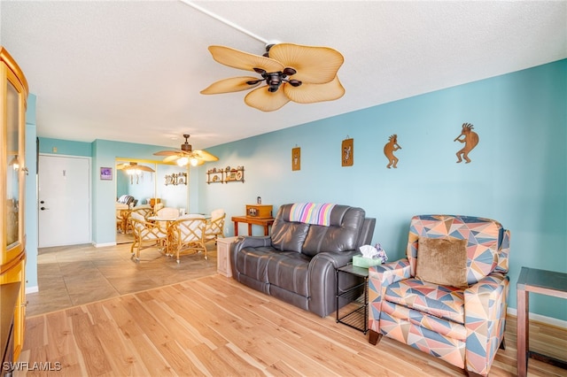 living room with light wood finished floors, ceiling fan, baseboards, and a textured ceiling