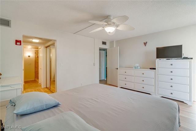 bedroom featuring a ceiling fan, visible vents, a textured ceiling, and light wood finished floors