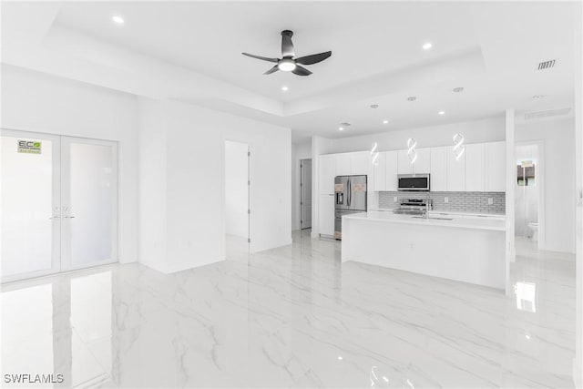 kitchen featuring white cabinets, a raised ceiling, an island with sink, decorative light fixtures, and stainless steel appliances