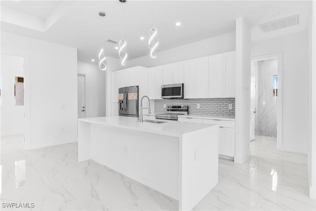 kitchen featuring decorative backsplash, stainless steel appliances, a kitchen island with sink, decorative light fixtures, and white cabinets