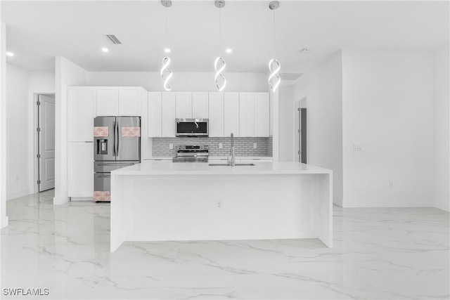 kitchen with appliances with stainless steel finishes, a kitchen island with sink, sink, white cabinetry, and hanging light fixtures