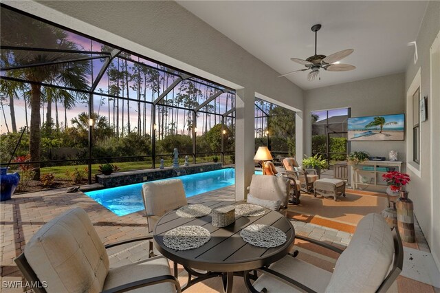 pool at dusk with a patio area, ceiling fan, and glass enclosure