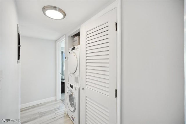 clothes washing area with light hardwood / wood-style floors and stacked washer / drying machine