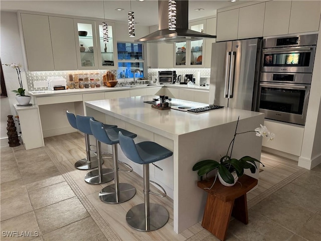 kitchen featuring island exhaust hood, stainless steel appliances, a center island, white cabinetry, and hanging light fixtures