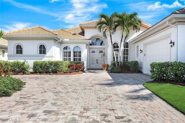 mediterranean / spanish-style home featuring a tile roof, driveway, an attached garage, and stucco siding