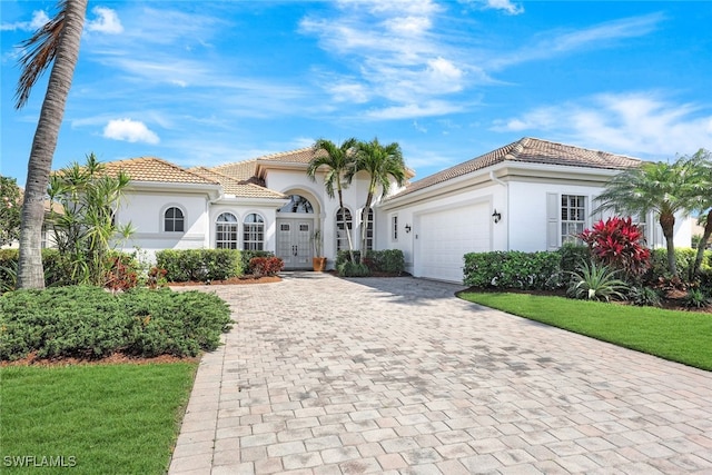 mediterranean / spanish-style home with decorative driveway, a tiled roof, an attached garage, and stucco siding