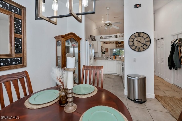 tiled dining space with ceiling fan with notable chandelier, sink, and a high ceiling