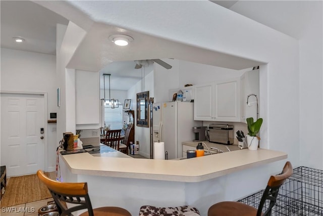 kitchen with lofted ceiling, white cabinets, white fridge with ice dispenser, decorative light fixtures, and kitchen peninsula