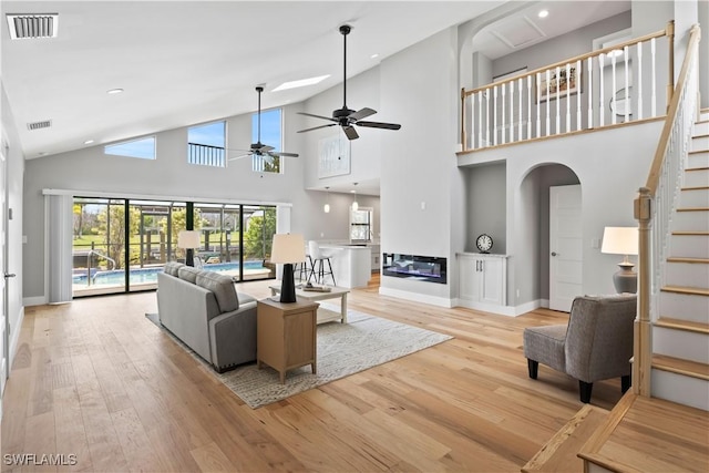 living room featuring ceiling fan, a towering ceiling, and light hardwood / wood-style flooring