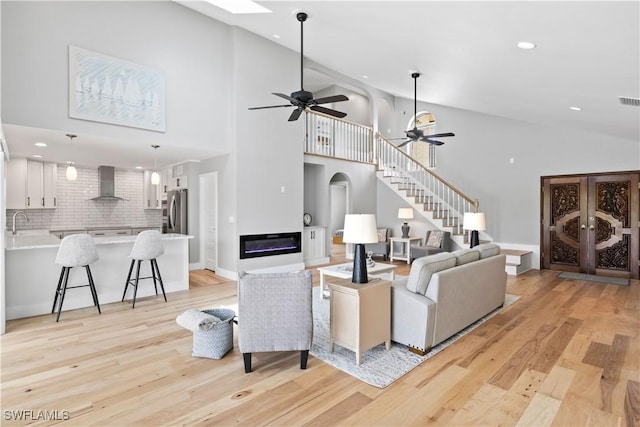 living room featuring ceiling fan, light hardwood / wood-style floors, sink, and high vaulted ceiling