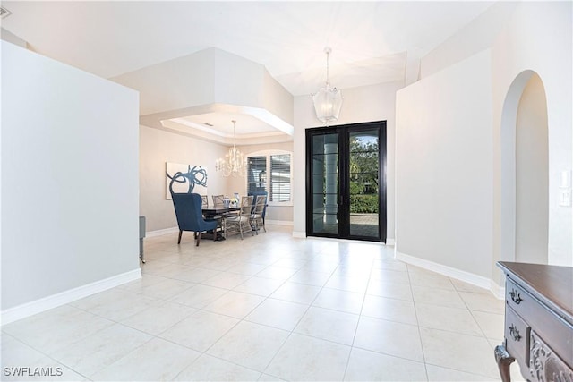 foyer entrance featuring light tile patterned floors, french doors, a tray ceiling, and an inviting chandelier