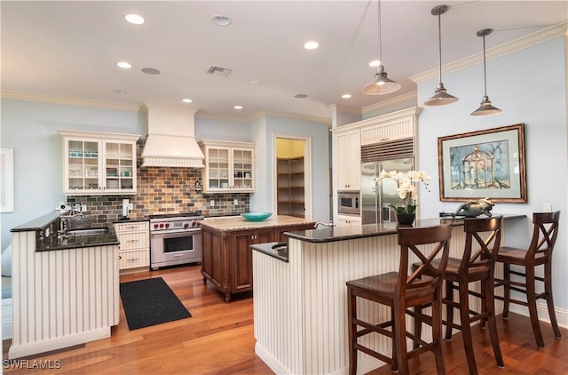 kitchen featuring decorative light fixtures, a kitchen breakfast bar, a center island, built in appliances, and custom range hood